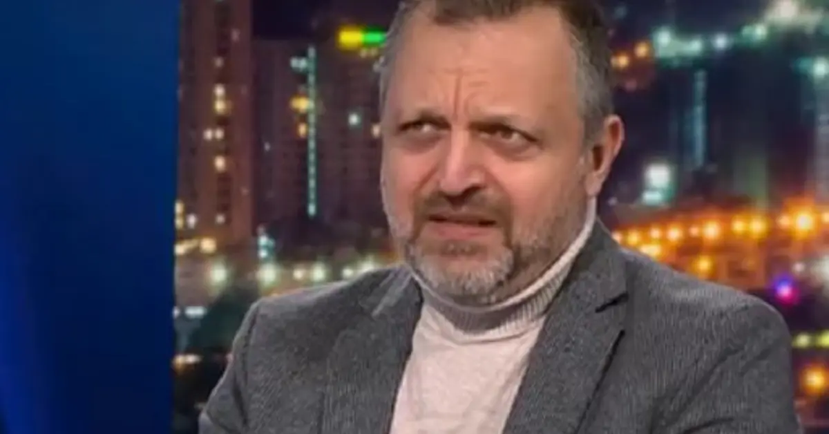 Нов обрат в убийството на Слави Бинев: Бивш висш кадър на МВР допуска скандал между познати, прераснал в смъртоносна стрелба Мъж с брада и сиво сако с поло блуза говори в телевизионно студио с градски светлини на заден план.