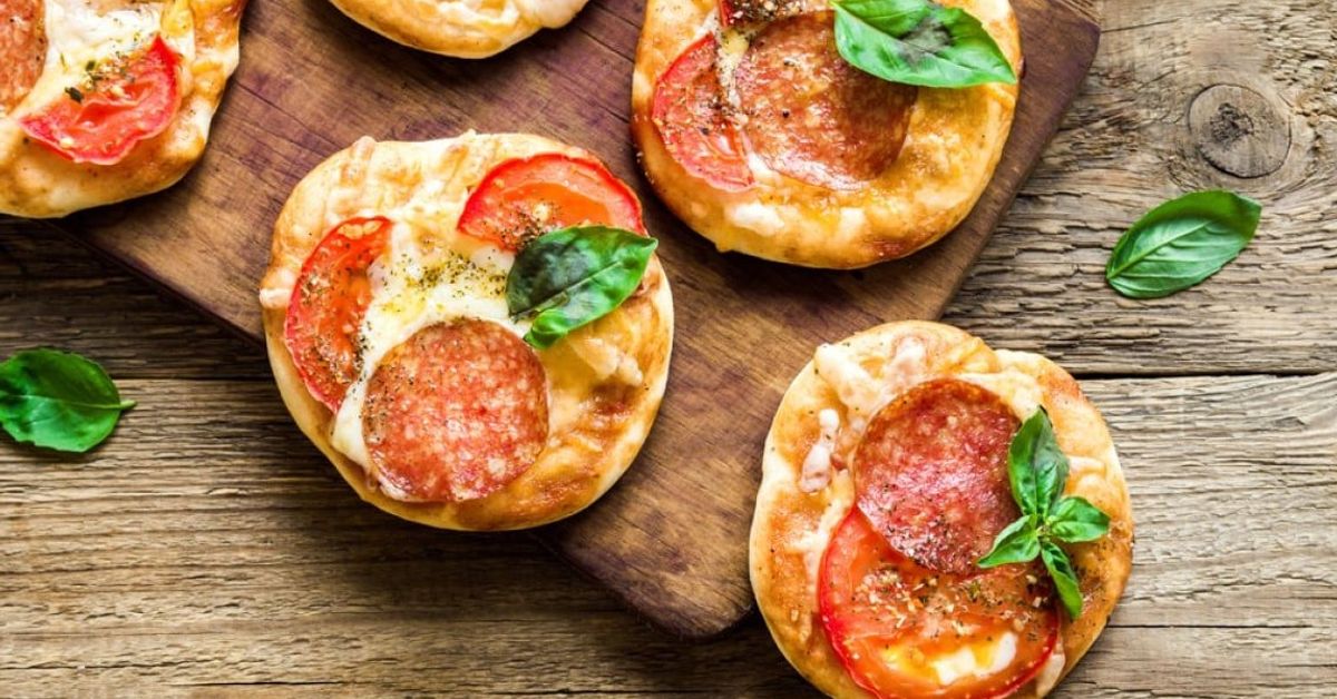 Ароматни домашни мини пици – класическа рецепта Вкусни мини пици с пеперони, сирене, домати и свеж босилек върху дърво.
