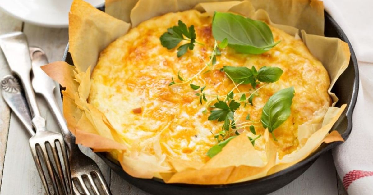 Най-вкусната баница с лук – проста рецепта с чудесен резултат Прясно изпечен златист киш с босилек и мащерка в черен тиган.