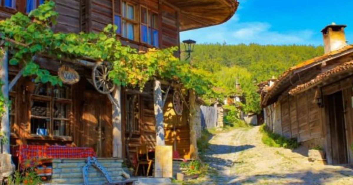 Тези 5 планински селища в България очароват с тишина и гледки (СНИМКИ) Живописна българска улица с традиционни дървени къщи и зелени лози.