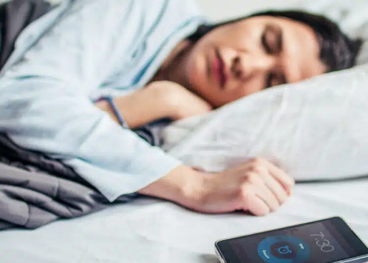 Woman Sleeping On Bed With Alarm On Mobile Phone