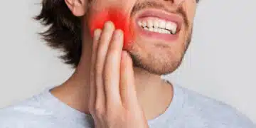 Tooth and gum inflammation. Guy suffers from pain in his mouth and presses hand to red sore spot, panorama, cropped, studio shot