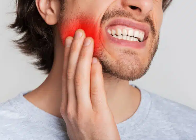 Tooth and gum inflammation. Guy suffers from pain in his mouth and presses hand to red sore spot, panorama, cropped, studio shot