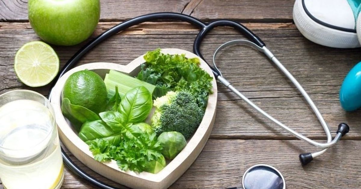 Ето какви продукти обича сърцето, ако искаме да го поддържаме здраво и в добра форма: Сърцевидна купа със зеленчуци, плодове, стетоскоп и спортни принадлежности за здраве.