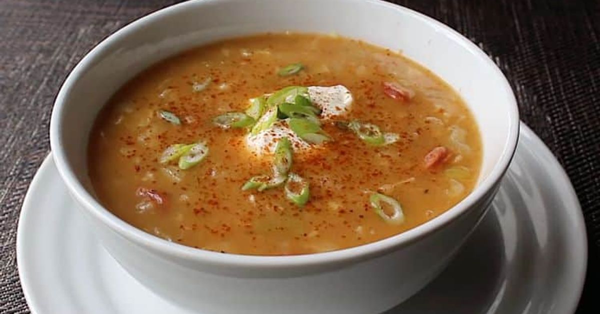 Невероятно вкусна унгарска супа с наденица – готова само за 20 минути Кремообразна супа в бяла купа, гарнирана със заквасена сметана, зелен лук и червен пипер.