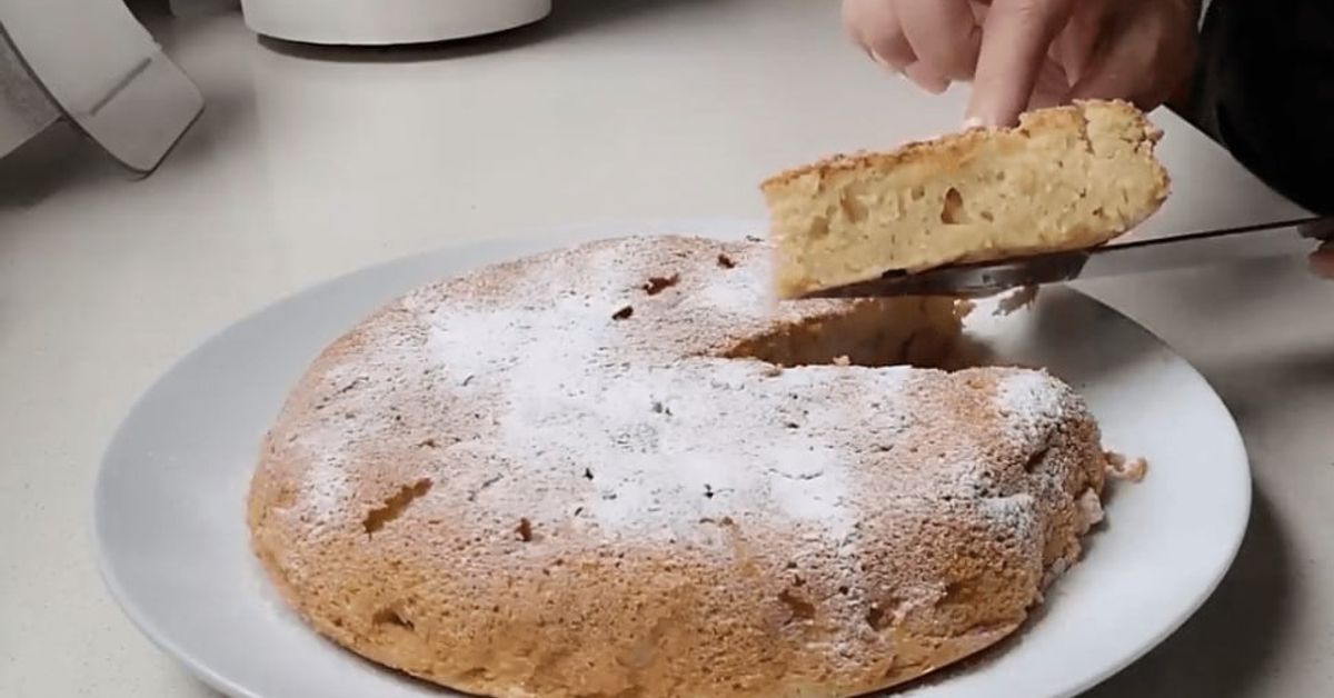Пухкав ябълков пай с прости продукти (Рецепта) Златист сладкиш с пудра захар, от който се взима парче за сервиране.