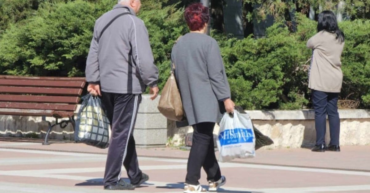 Какво трябва да знаем за пенсиите при пълен и непълен осигурителен стаж, както и за пенсиите в намален размер Възрастна двойка се разхожда с пазарски торби в слънчев градски парк.