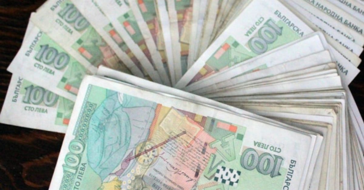 3 милиона души ще плащат повече пари за пенсия, за да може да влязат още 611 милиона лева в НОИ Много български банкноти от 100 лева, разпръснати на тъмна дървена маса.