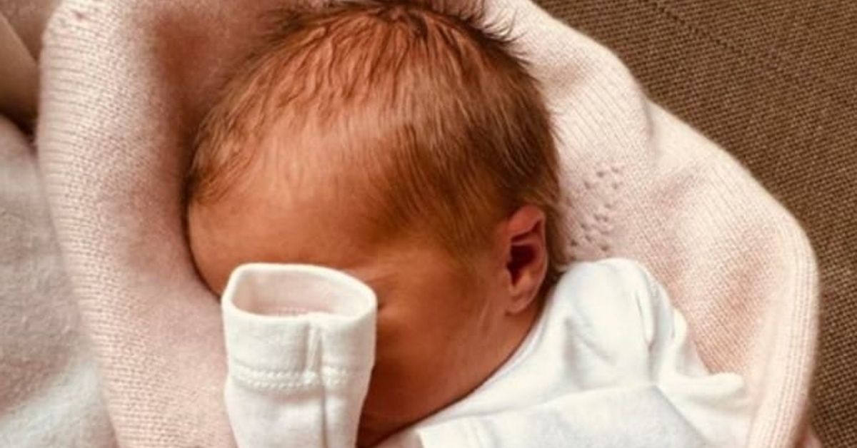 Щастие в кралското семейство – роди се още едно бебенце! Спящо новородено бебе с червеникава коса, увито в плетено розово одеяло.
