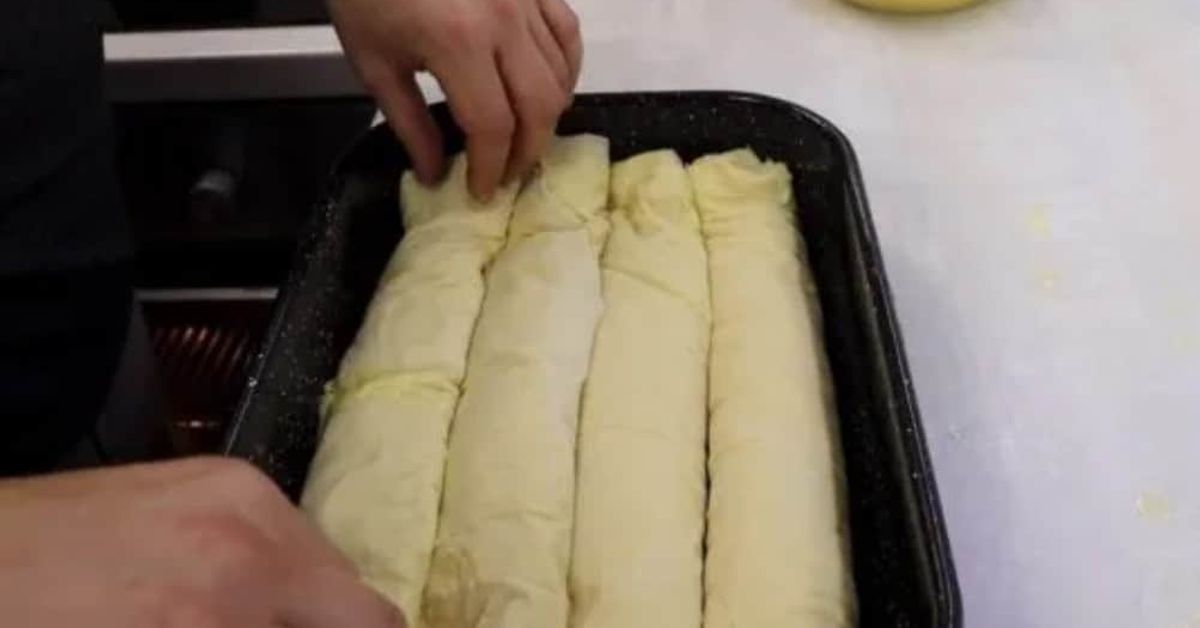 Става като пух: вкусна баница с готови кори и уникална заливка (Рецепта) Приготвяне на баница: ръце подреждат навити кори в тава за печене.
