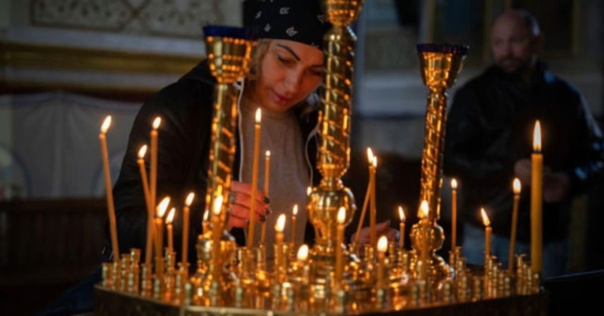 Днес, 3 януари е Църковен празник – имен ден имат много българи, а суеверята гласят, че е лош ден и за какво да внимаваме! Жена пали молитвени свещи пред златен свещник в църква.