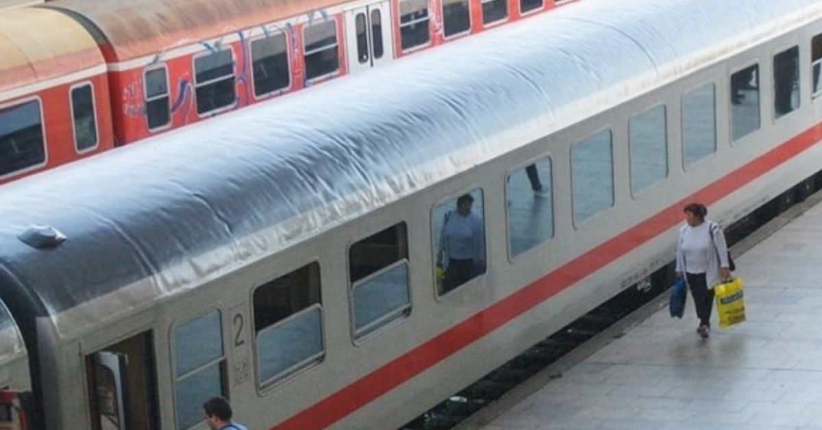 Заради смяната на времето БДЖ променят разписанието на влаковете Жена върви по перона до сребрист влак, червен влак е на заден план.