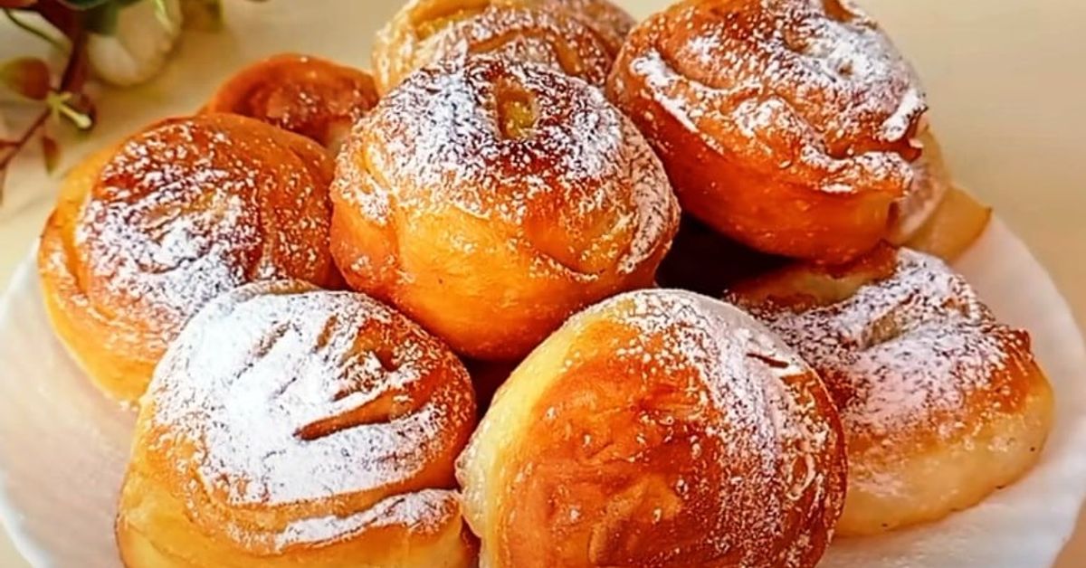 Готвя ябълкова вкусотия в тиган, за да е хрупкава коричката, а вътре да има море от крехък пълнеж... любим десерт! Апетитни златисти сладкиши, поръсени с пудра захар на бяла чиния.