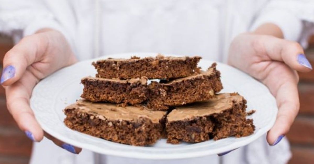 Рецепта за брауни с тиквички: Вкус, който ще ви изненада Ръце държат бяла чиния с няколко парчета шоколадови браунита с глазура.