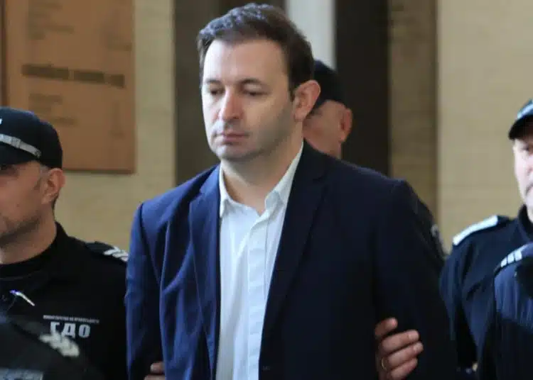 Задържан мъж, охраняван от полиция.