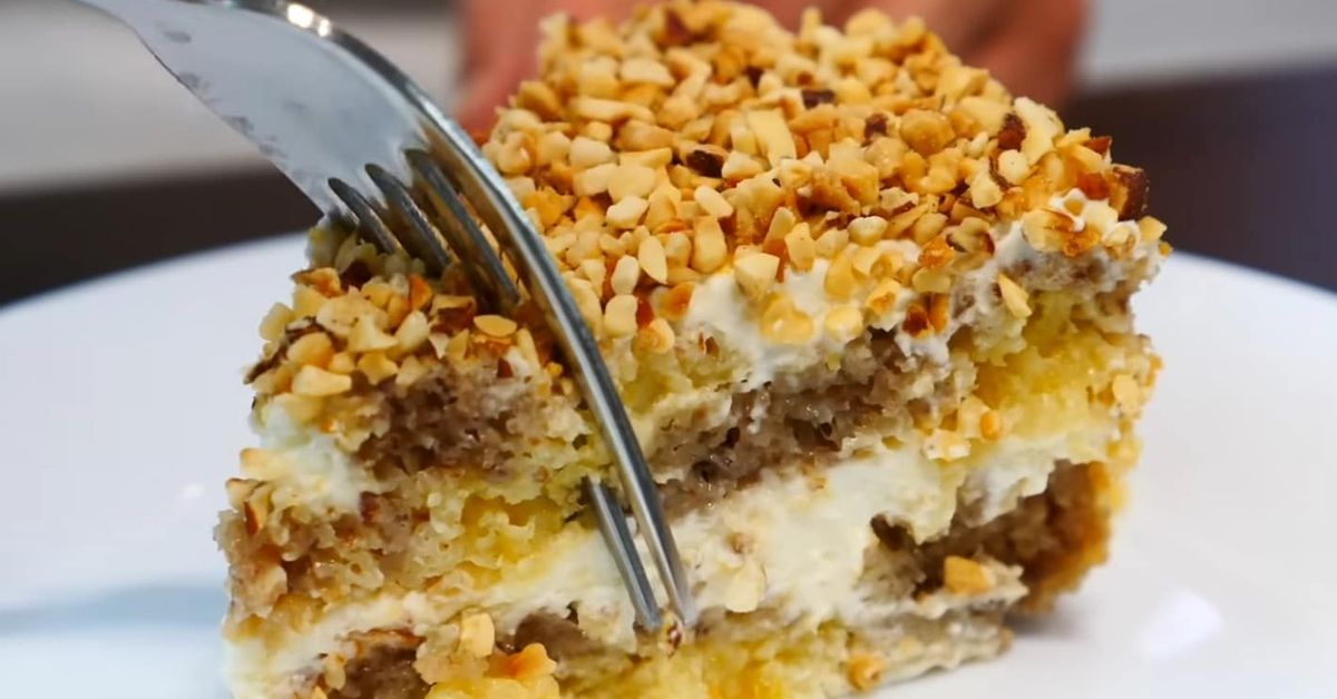 Домашна лимонова торта: Най-вкусният празничен десерт Многослойна торта с ядки и крем, разрязвана с вилица на бяла чиния.