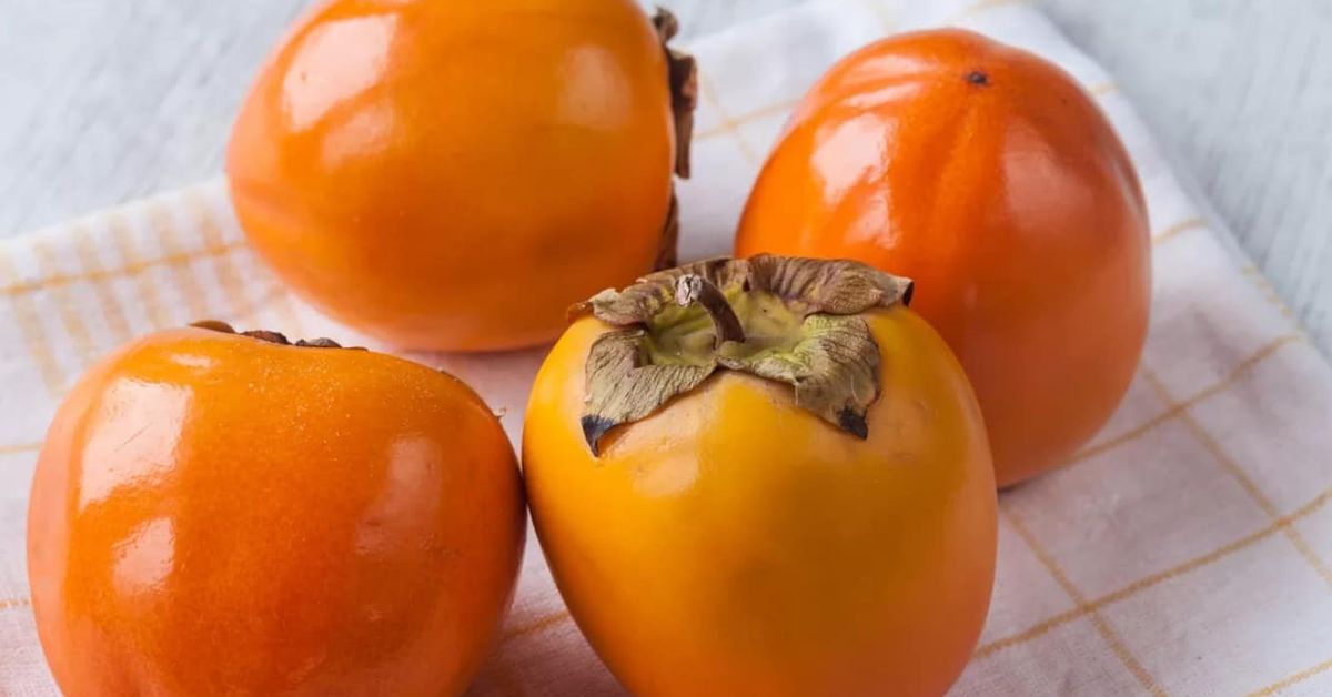 Как да си приготвим печена райска ябълка с подправки – вкусен десерт за 30 минути Четири зрели райски ябълки с дръжки върху бяла кухненска кърпа.